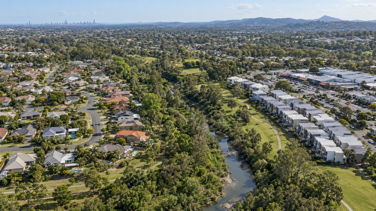 Aerial view of a South East Queensland suburb showing detached houses, townhouses, a creek parkland corridor and local shops