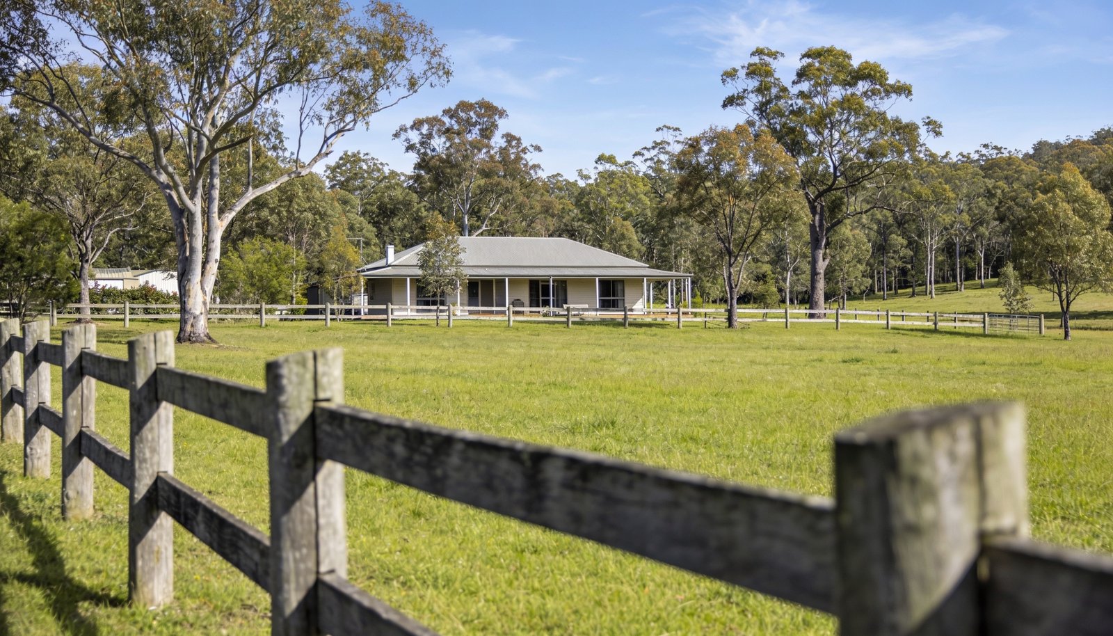 Semi-rural Queensland acreage property with a single-storey farmhouse, post-and-rail fencing and a grassy paddock with gum trees