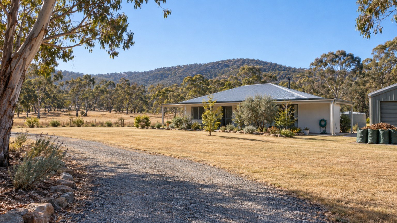Homeowner clearing leaf litter and trimming vegetation around a semi-rural Australian house before fire season